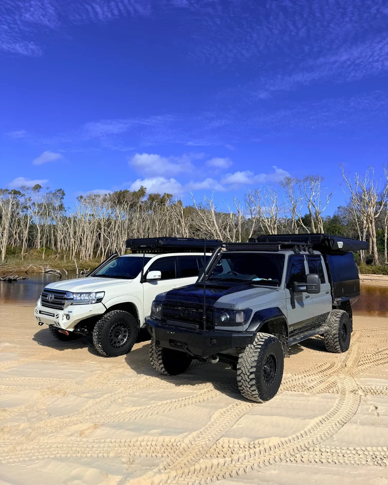 The 200 Series and Drewsy's 79 side by side on the sand at Straddie, rooftop tents packed on the racks.