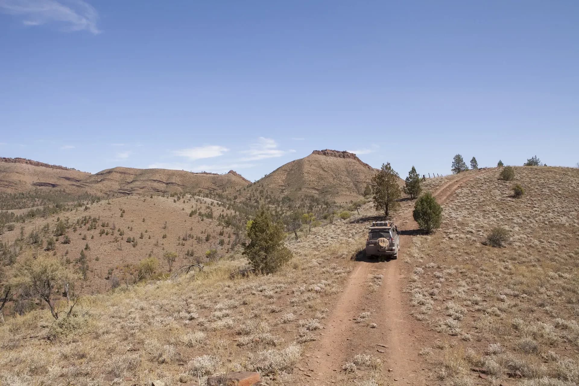 A 4x4 on a dirt track winding through dry hills.
