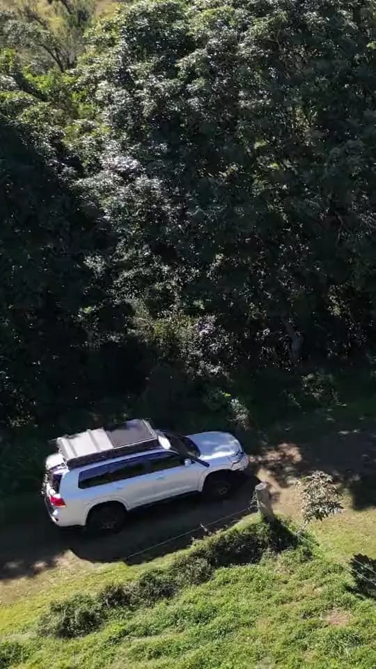 Drone view following a 79 Series and a 200 Series across a grassy paddock to camp.